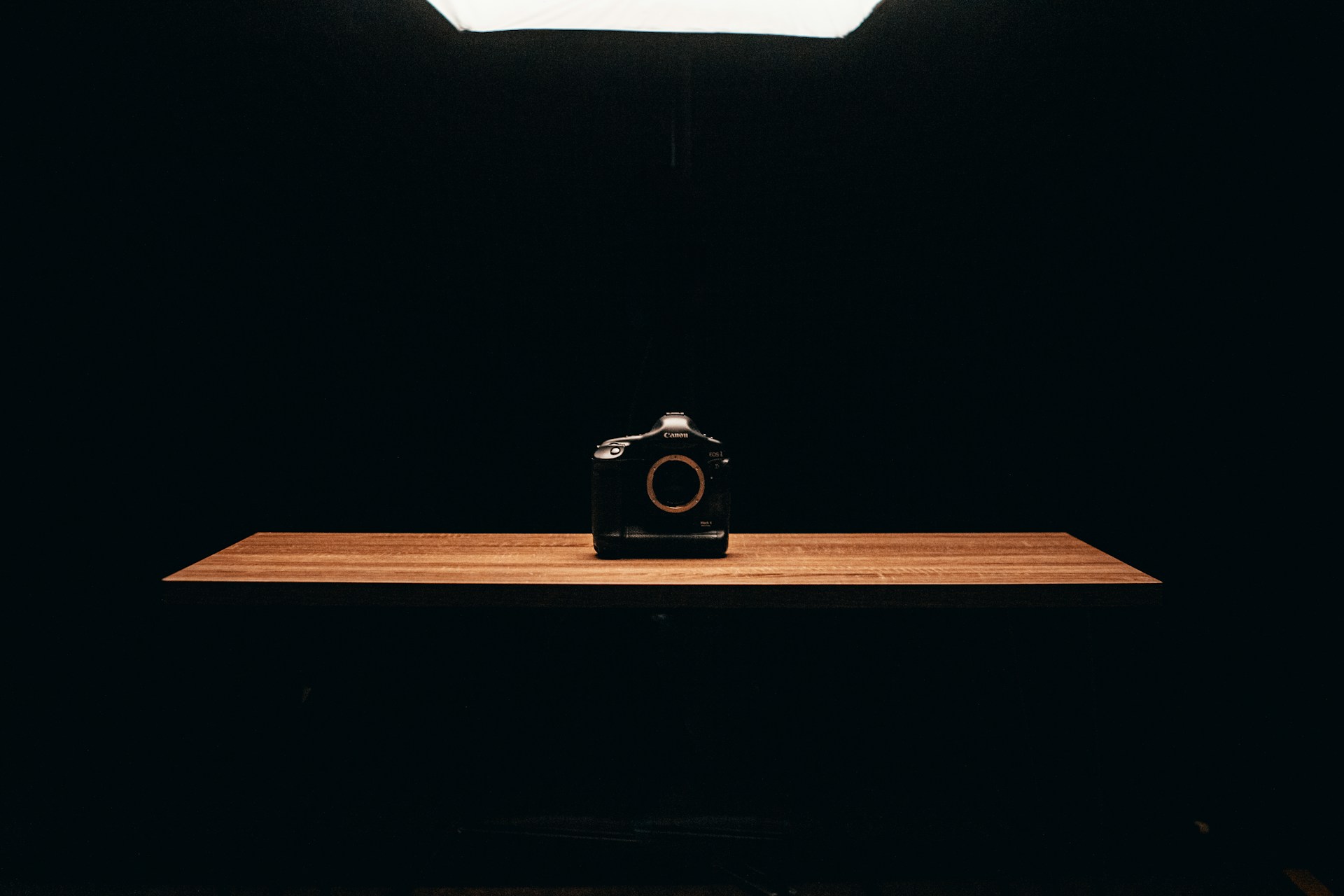 A black Canon camera sits centered on a wooden table against a dark background