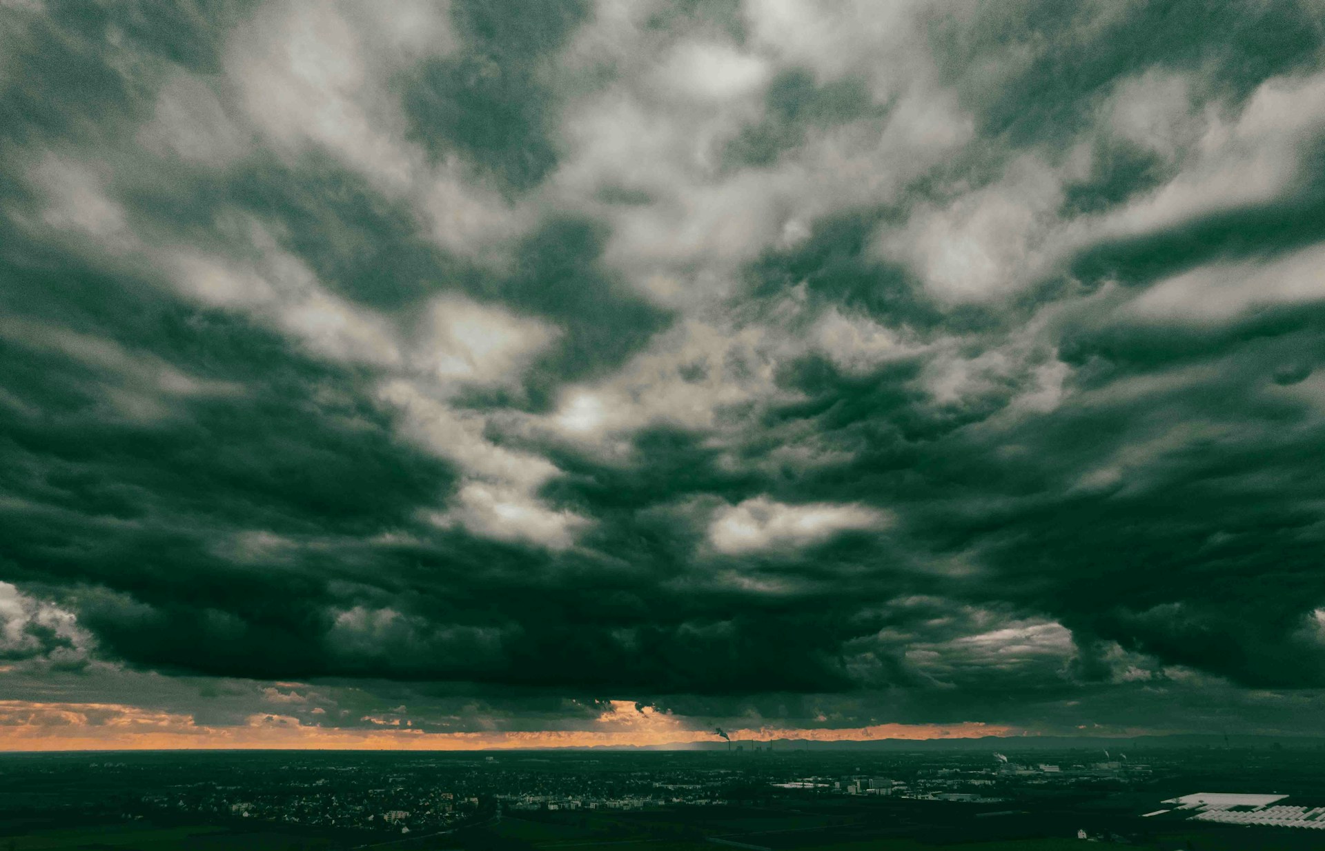 Dark storm clouds loom over a city with a hint of golden light on the horizon